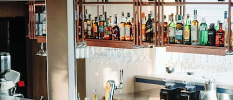 Un área de bar moderna con taburetes blancos, una barra larga y una variedad de botellas y copas.