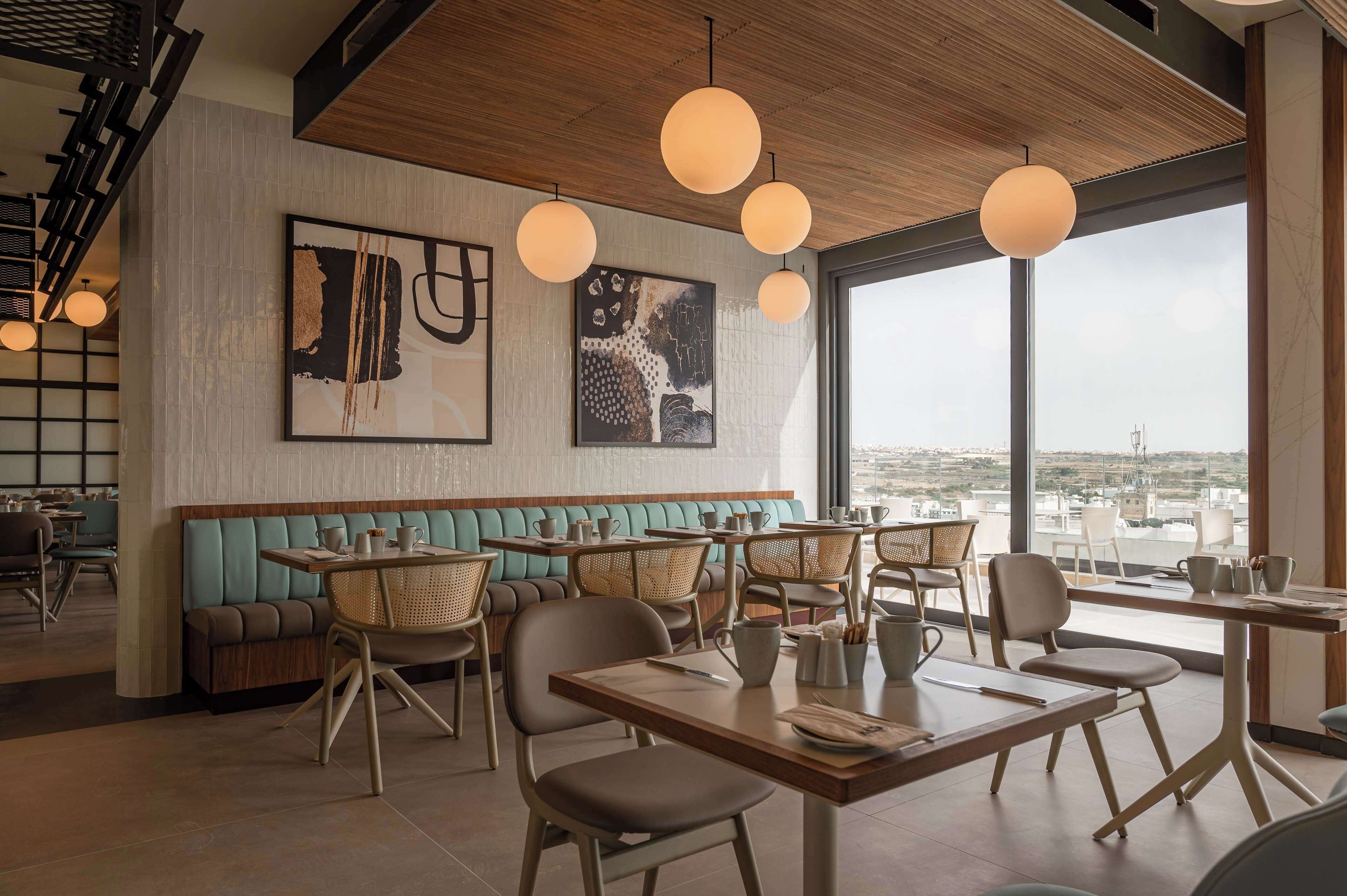 A modern restaurant interior with wooden ceiling, large windows, and artwork on the walls.