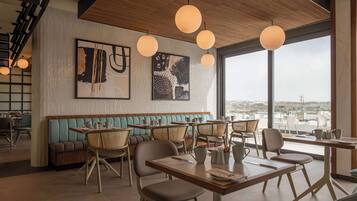 Un interior de restaurante moderno con techo de madera, ventanas amplias y obras de arte en las paredes.