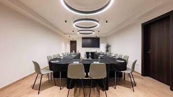 Une salle de conférence équipée d’une table ronde, de chaises, d’un téléviseur à écran plat et de luminaires circulaires au plafond.