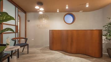 Un área de recepción con un mostrador de madera, una silla, una planta en maceta y el logotipo de Dee Spas Wellness montado en la pared.