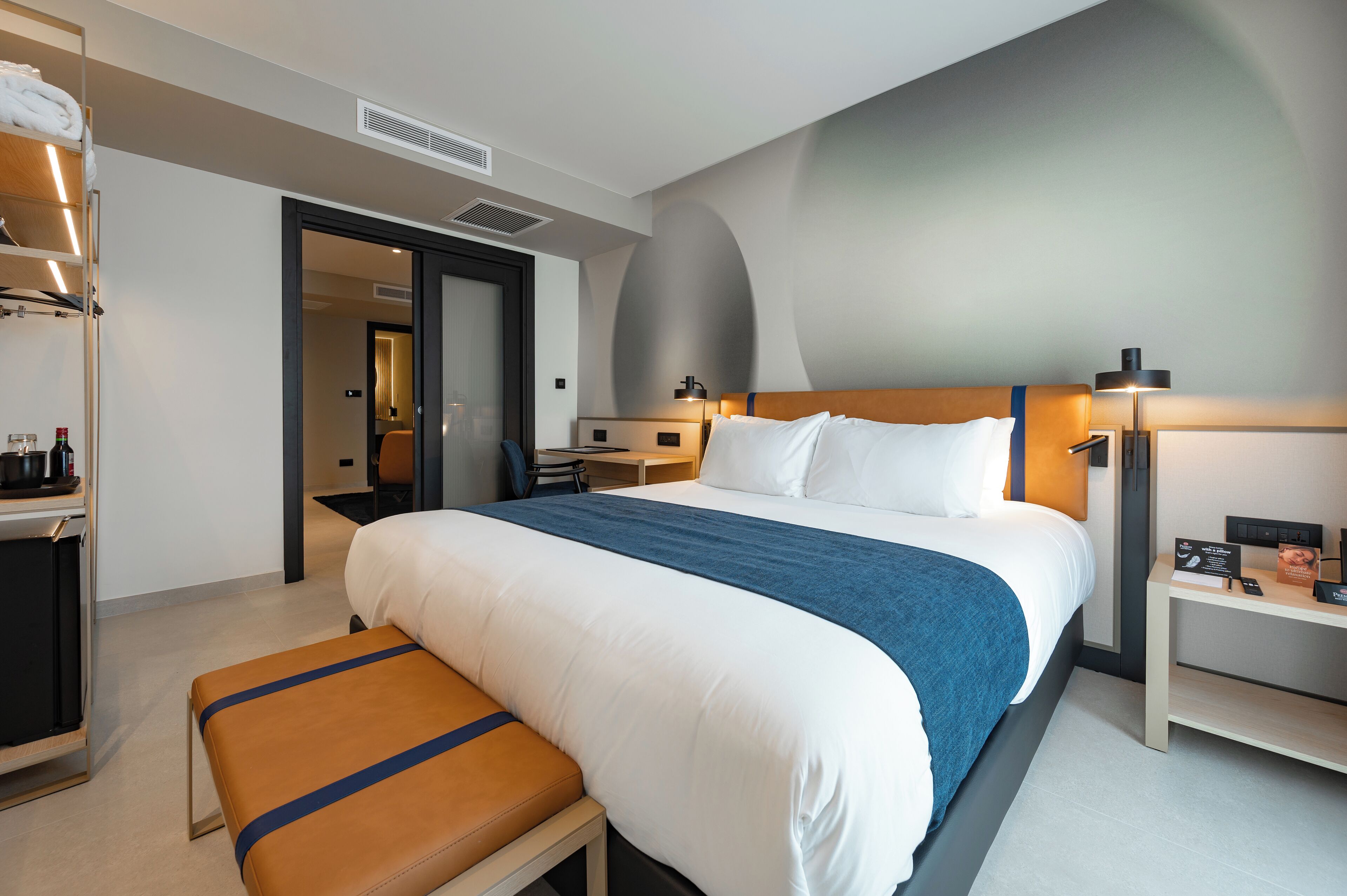 Una habitación de hotel moderna con una cama grande, un banco, un escritorio y un armario.