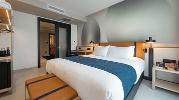Una habitación de hotel moderna con una cama grande, un banco, un escritorio y un armario.