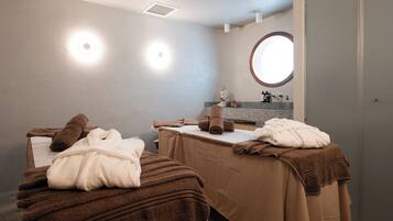 A spa room with two massage tables, towels, a mirror, and a sink.
