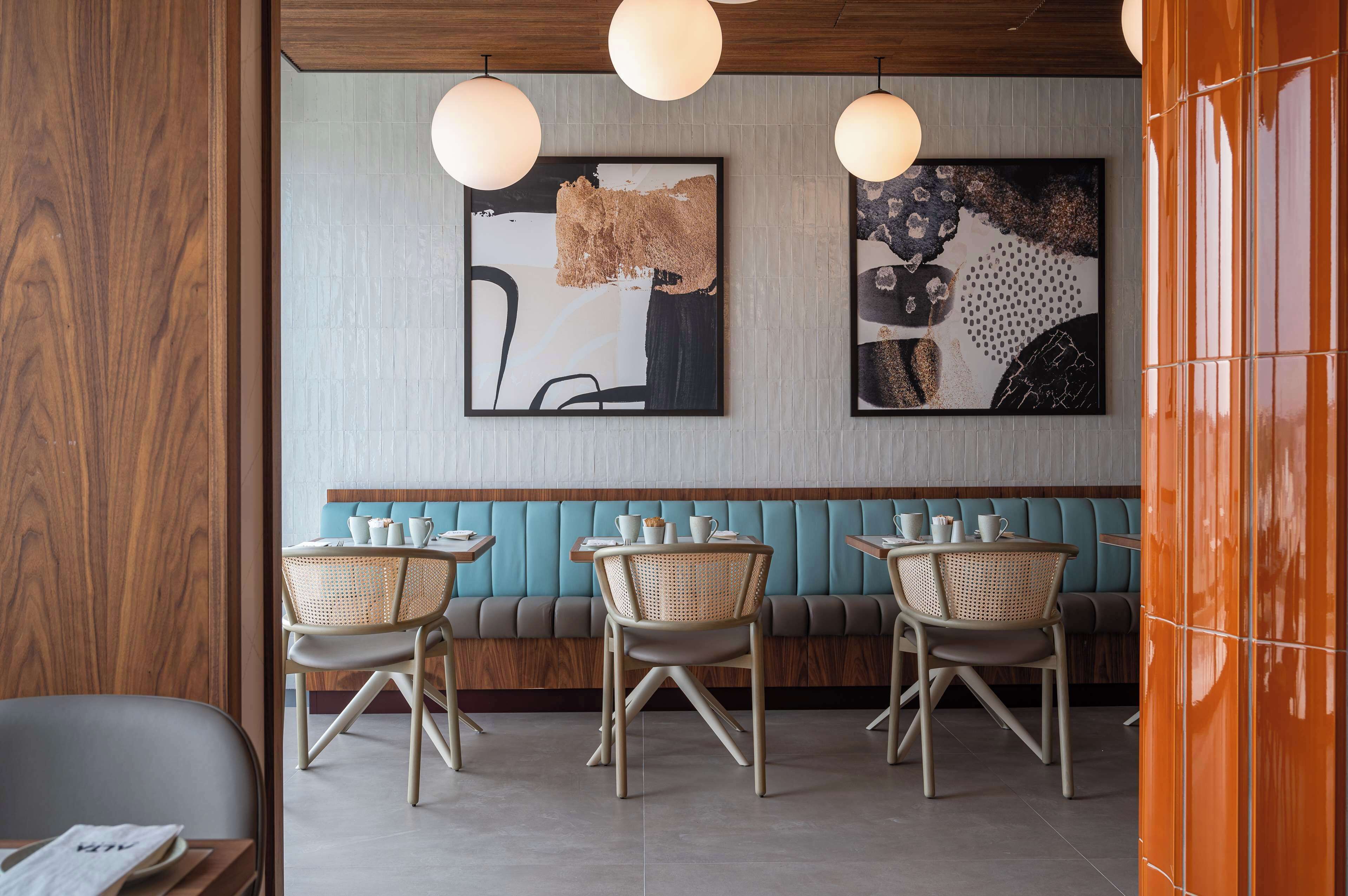 A restaurant interior with a wooden wall, teal cushioned bench seating, and wicker chairs.