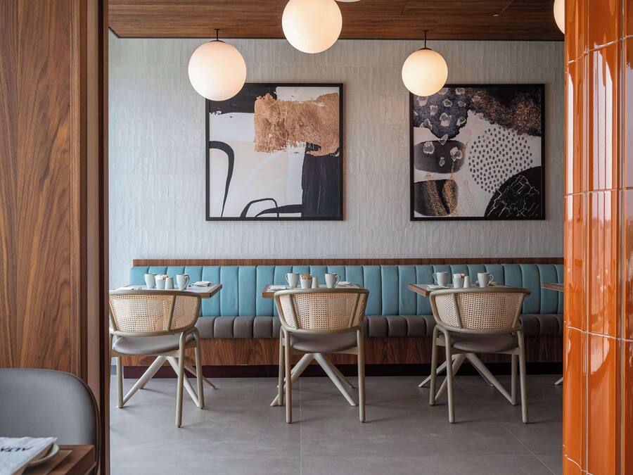A restaurant interior with a wooden wall, teal cushioned bench seating, and wicker chairs.