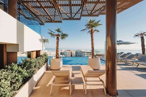 A rooftop pool area with lounge chairs, palm trees, and a view of the city.