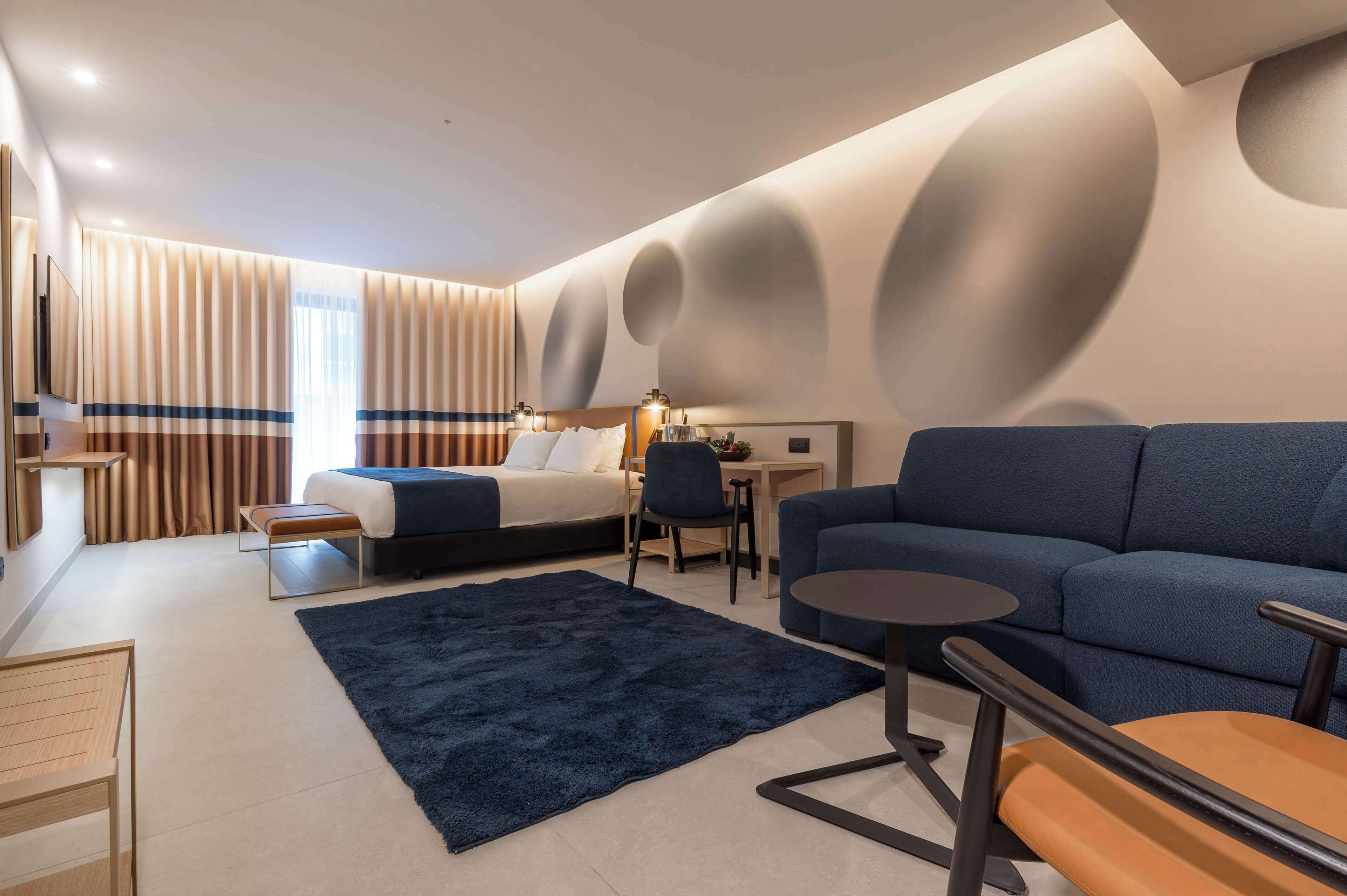 Una habitación de hotel moderna con cama, sofá, escritorio y una alfombra grande.