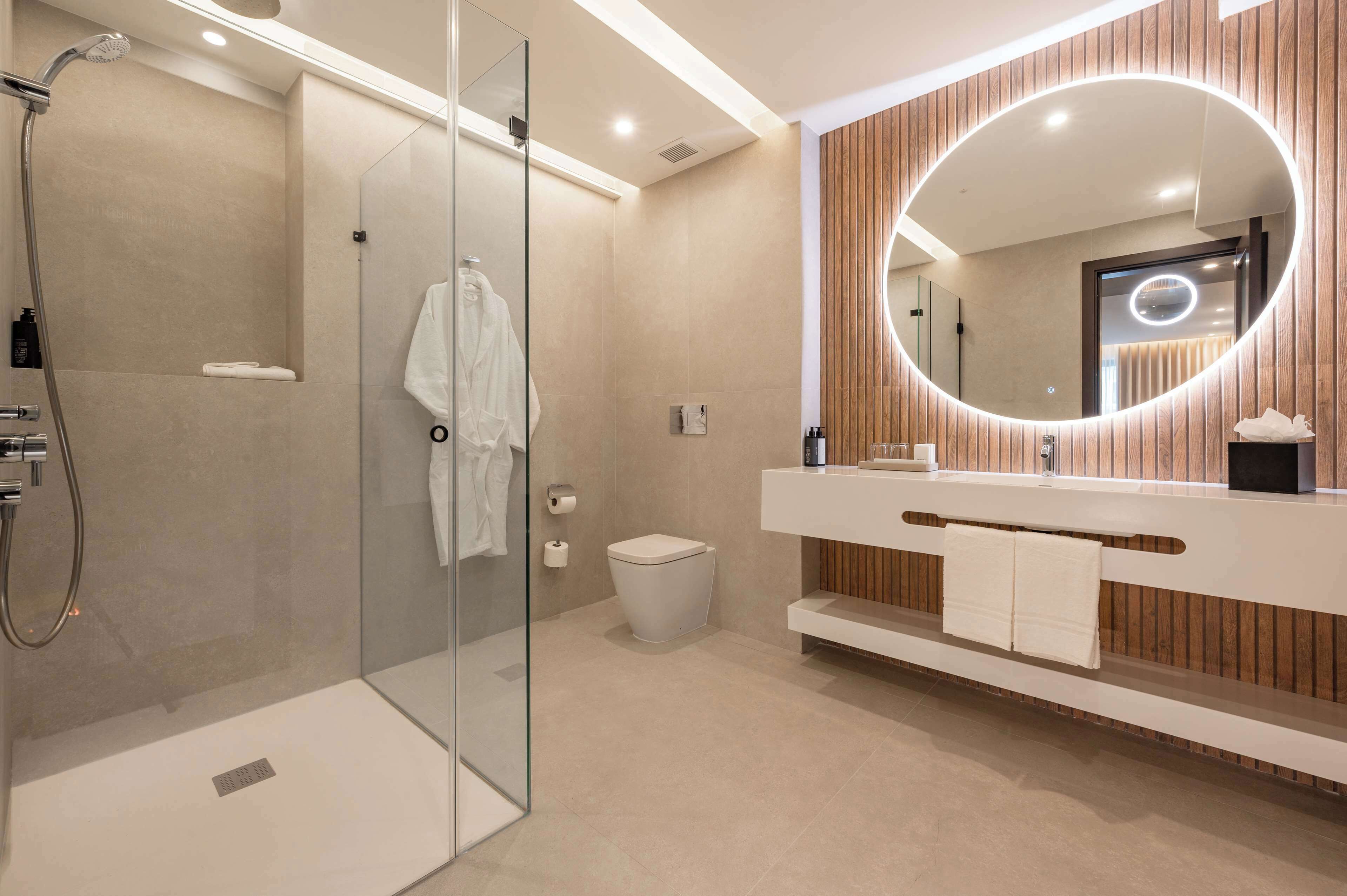 Un baño moderno con cabina de ducha de vidrio, inodoro, tocador con espejo y toallero.