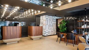 A modern reception area with wooden reception desks, a large potted plant, and a black wall with geometric patterns.