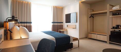 A modern hotel room with a bed, bedside table, lamp, and a view of the city.