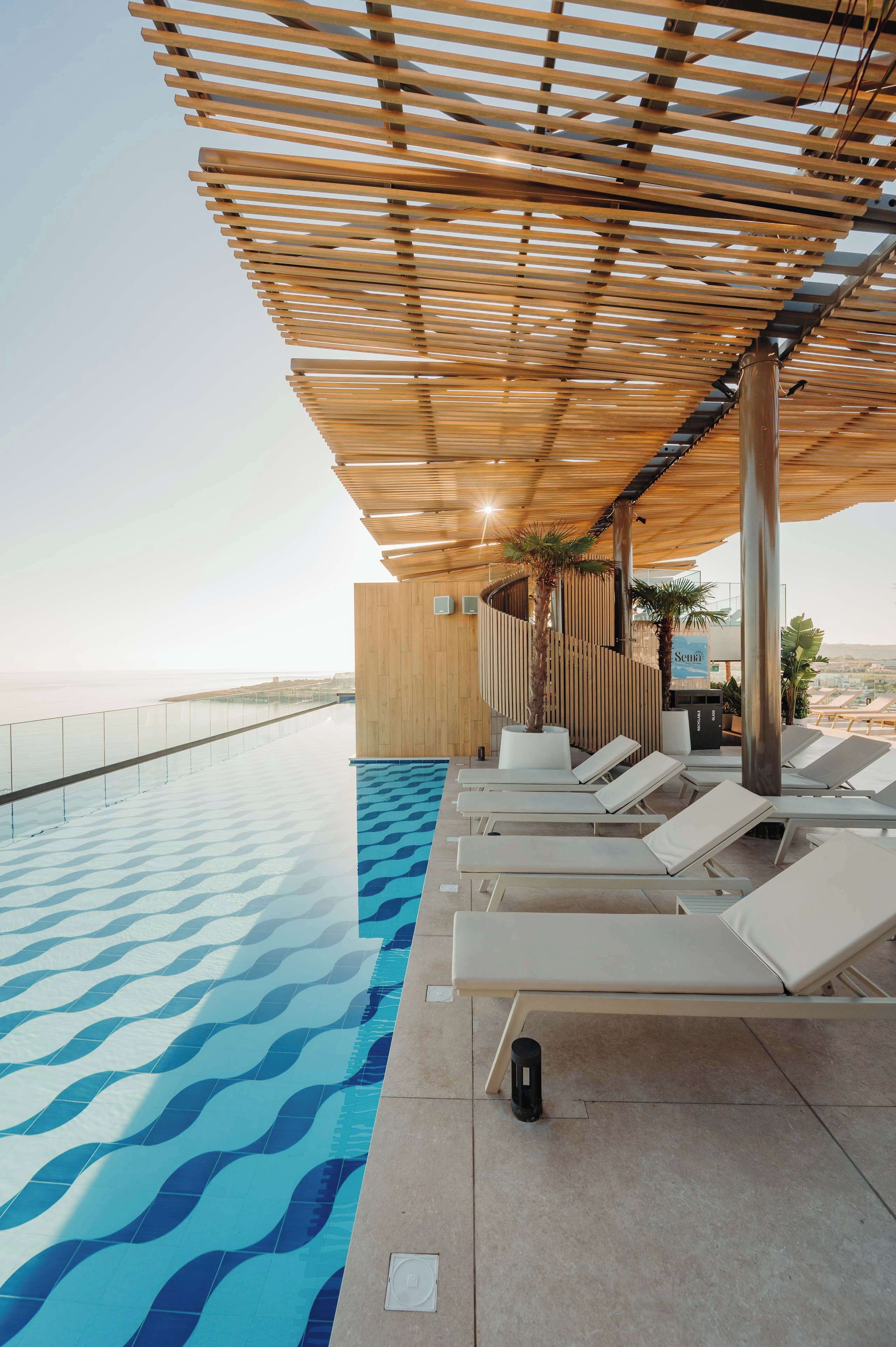 A poolside area with lounge chairs, a wooden pergola, and a view of the sea.