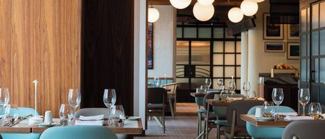 A restaurant interior with tables set for dining, hanging spherical light fixtures, and a brick floor.