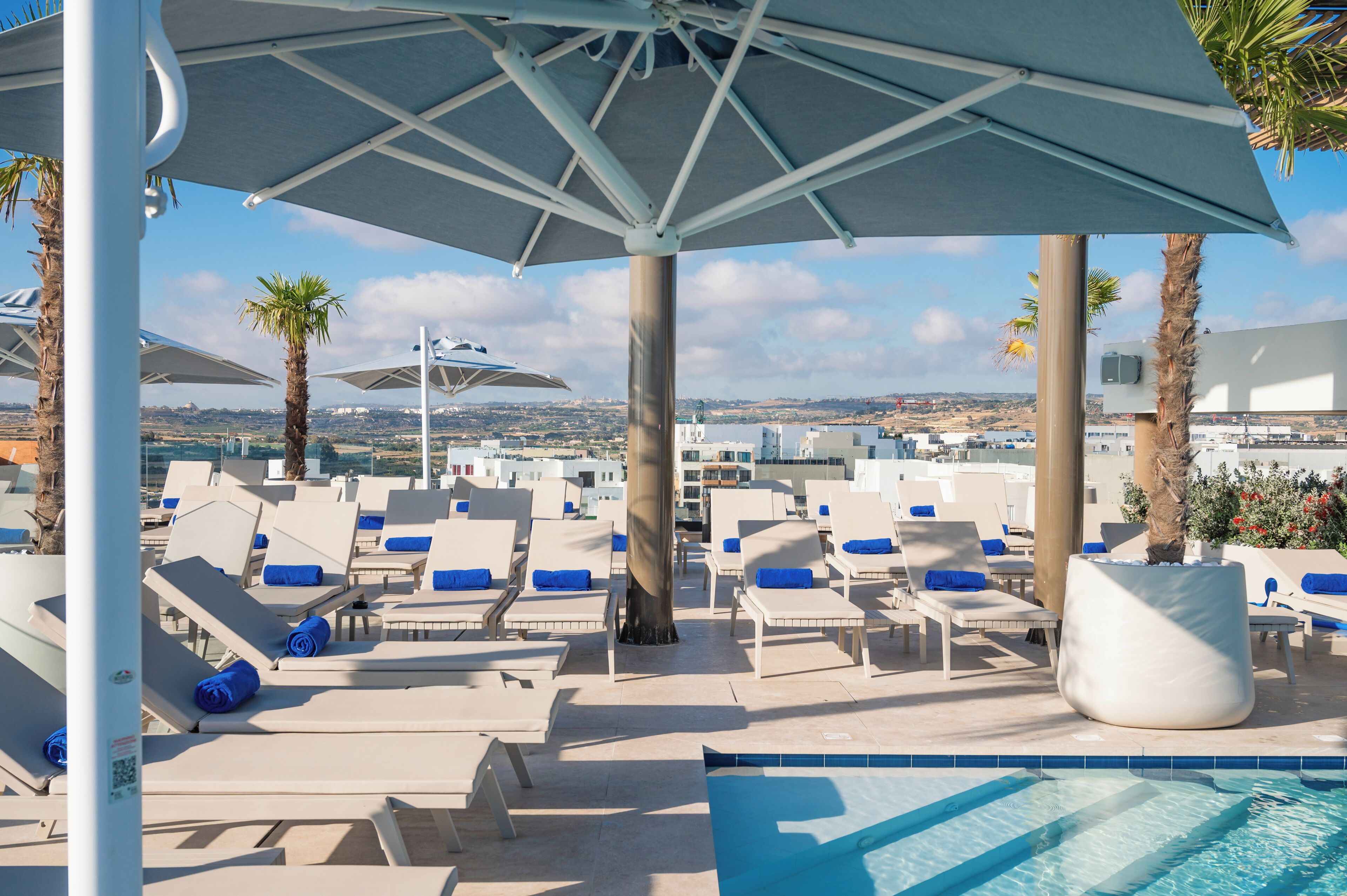 Un espace aménagé au bord de la piscine, avec des chaises longues, des parasols et une vue sur la ville.
