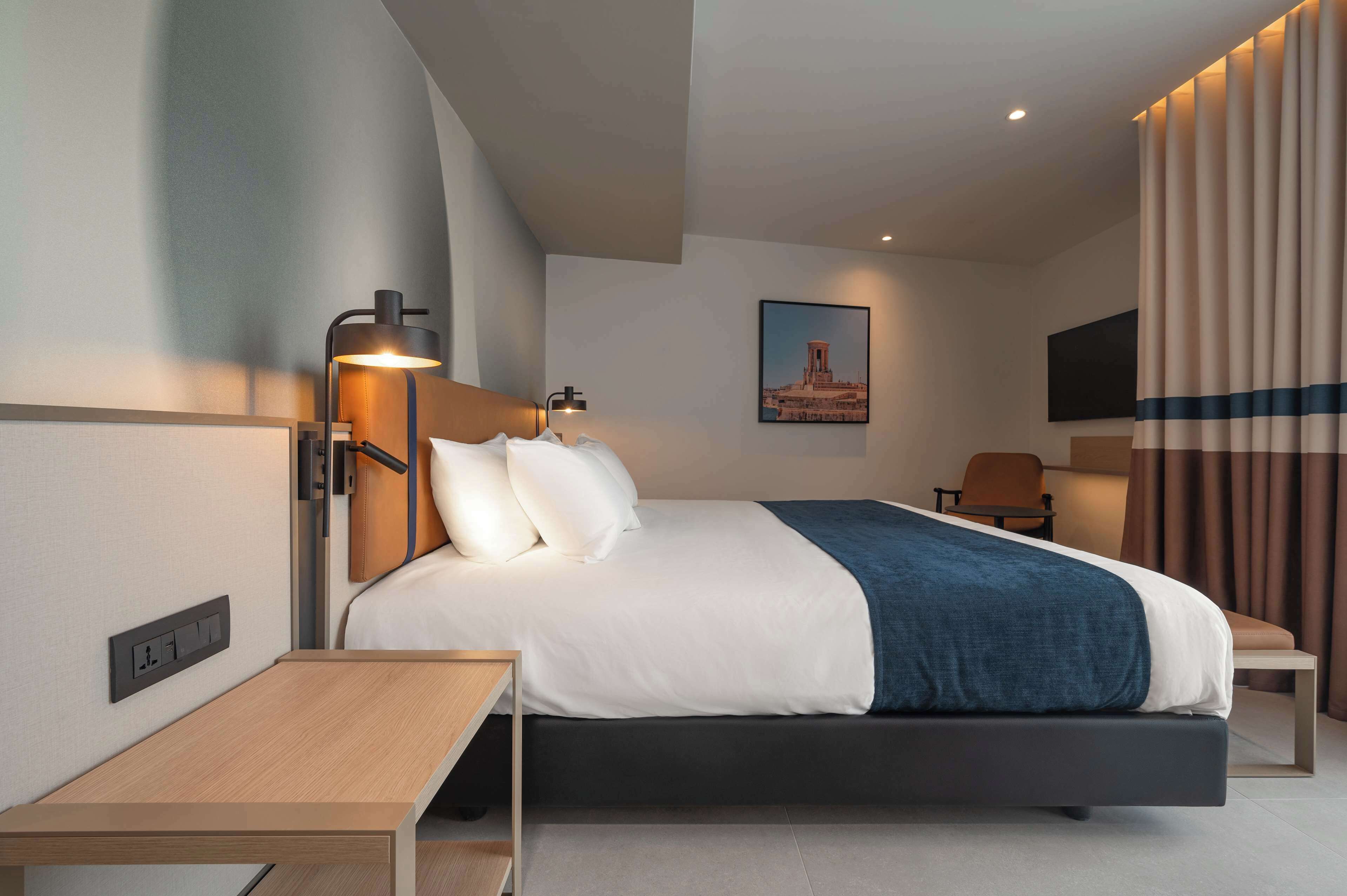 Une chambre d’hôtel moderne avec un lit, une table de chevet, une lampe et un tableau au mur.