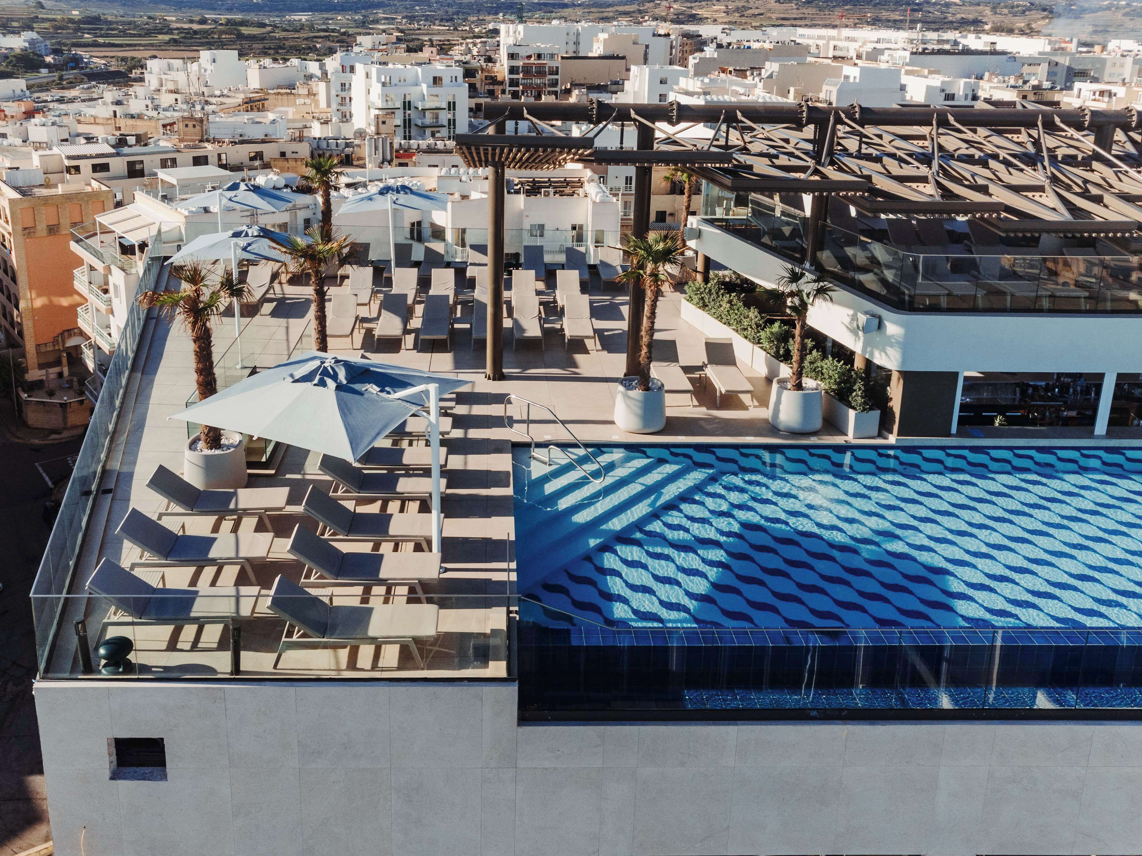 A rooftop pool area with lounge chairs and umbrellas, surrounded by buildings.