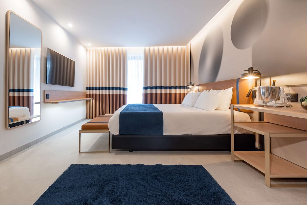 A modern hotel room with a large bed, bedside tables, a desk, and a mirror.
