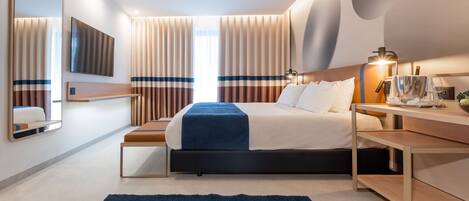 A modern hotel room with a large bed, bedside tables, a desk, and a mirror.