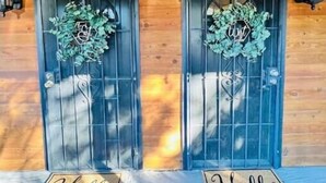 L’entrée d’un chalet en bois, avec deux portails en métal, chacun orné d’une guirlande et d’un paillasson sur lequel est écrit « Bonjour ».