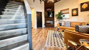 Un escalier mène à un espace de vie doté d’un plancher en bois, d’un canapé, d’une table basse et d’un ventilateur de plafond.
