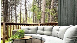 Un espace extérieur aménagé avec un coin salon abrité, comprenant un canapé incurvé, une petite table ronde et un tapis à motifs.