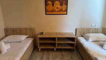 A room with two single beds, a wooden nightstand with a remote control, and a framed picture on the wall.