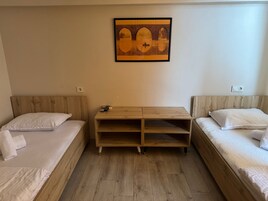 A room with two single beds, a wooden nightstand with a remote control, and a framed picture on the wall.