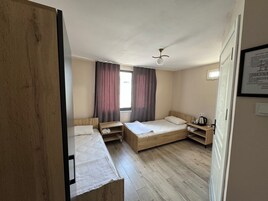 Habitación de hotel con dos camas individuales, cabecera de madera, una mesita pequeña, una mesita de noche, una ventana con cortinas y un ventilador de techo.