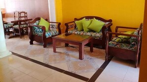 A room with a yellow wall, a wooden sofa set with green cushions, a matching armchair, and a coffee table. - Beautiful Casa De Rose (Progreso)