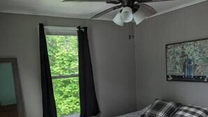 A bedroom with a bed, a ceiling fan, a window with curtains, and a painting on the wall. - Home Away From Home (Biggsville)
