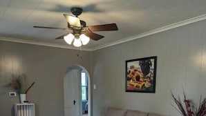 A living room with a grey sofa, a blue armchair, a wooden floor, a ceiling fan, and a painting on the wall. - Home Away From Home (Biggsville)