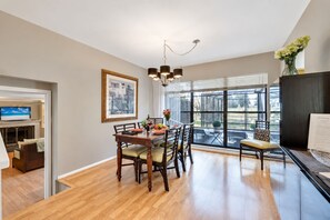 A dining area with a wooden table, chairs, a chandelier, and a view through large windows.
