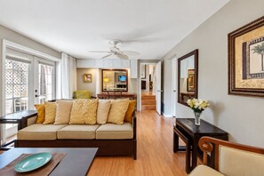 A living room with a sofa, a dining table, and a TV in the background. - Stunning Home w/ Heated Saltwater Pool & Pond View + 12 Guests + Great Location (Temple Terrace)
