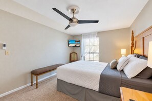 A hotel room with a bed, a bench, a ceiling fan, a TV, and a window with curtains. - Stunning Home w/ Heated Saltwater Pool & Pond View + 12 Guests + Great Location (Temple Terrace)