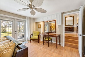 A room with a dining table, chairs, a sofa, a ceiling fan, and a view through a glass door.