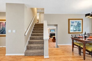 A staircase leading to a living area with a fireplace, a dining table with chairs, and a framed picture on the wall. - Stunning Home w/ Heated Saltwater Pool & Pond View + 12 Guests + Great Location (Temple Terrace)
