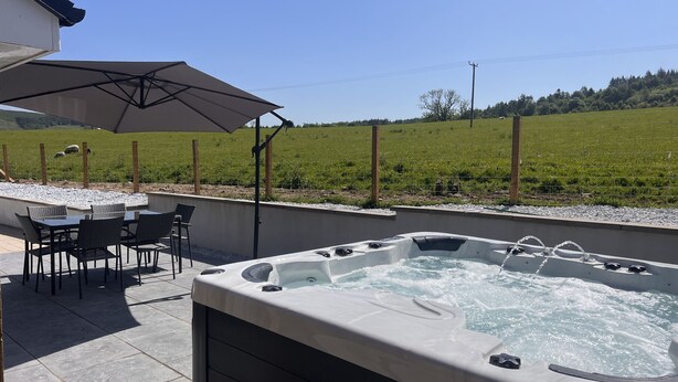 Un jacuzzi con mesa y sillas, rodeado por un patio con vistas a un campo verde.