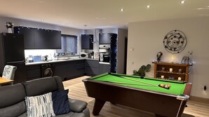 Una sala de estar moderna con billar, un sofá y una cocina al fondo.