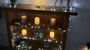 Una repisa de madera con múltiples velas encendidas y luces de cadena, decorada con una figurita de ciervo y un árbol de Navidad.