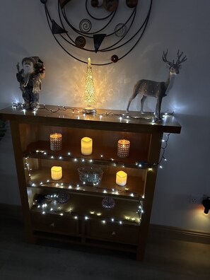 Adorned with string lights and candles, this display cabinet showcases a decorative tree and a deer figurine.