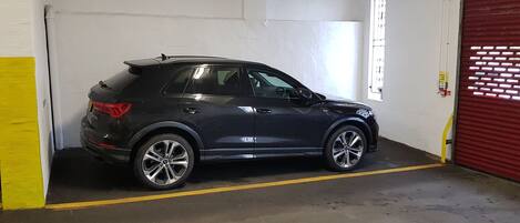 A black SUV parked inside a garage with a yellow line on the floor, a red garage door, and a white wall with a window.