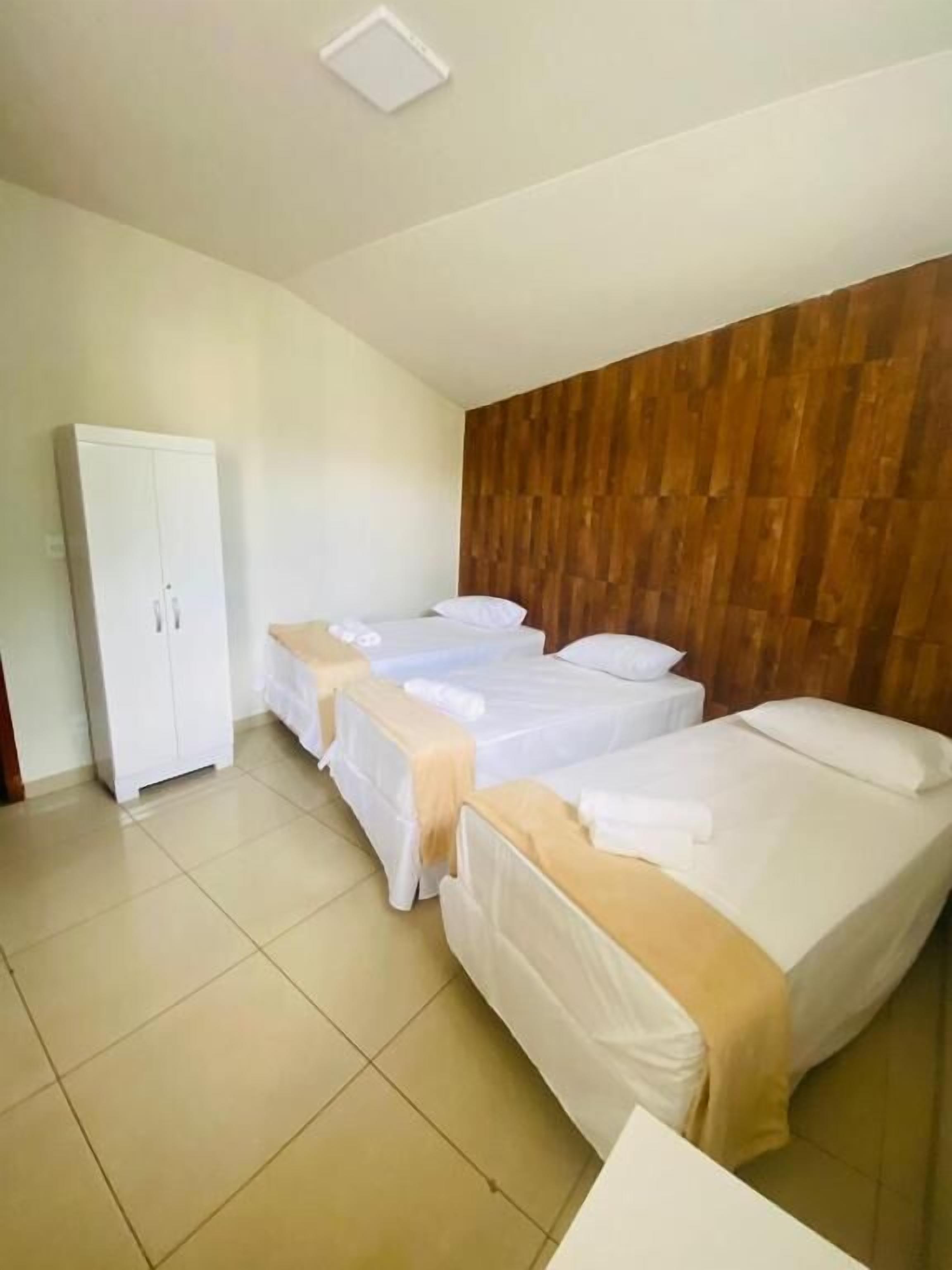 Habitación de hotel con tres camas, un armario y una pared de madera.