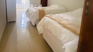 A hotel room with two beds, a small desk, and a door leading to another room.