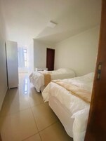 Quarto de hotel com duas camas, uma pequena escrivaninha e uma porta que dá para outro espaço.