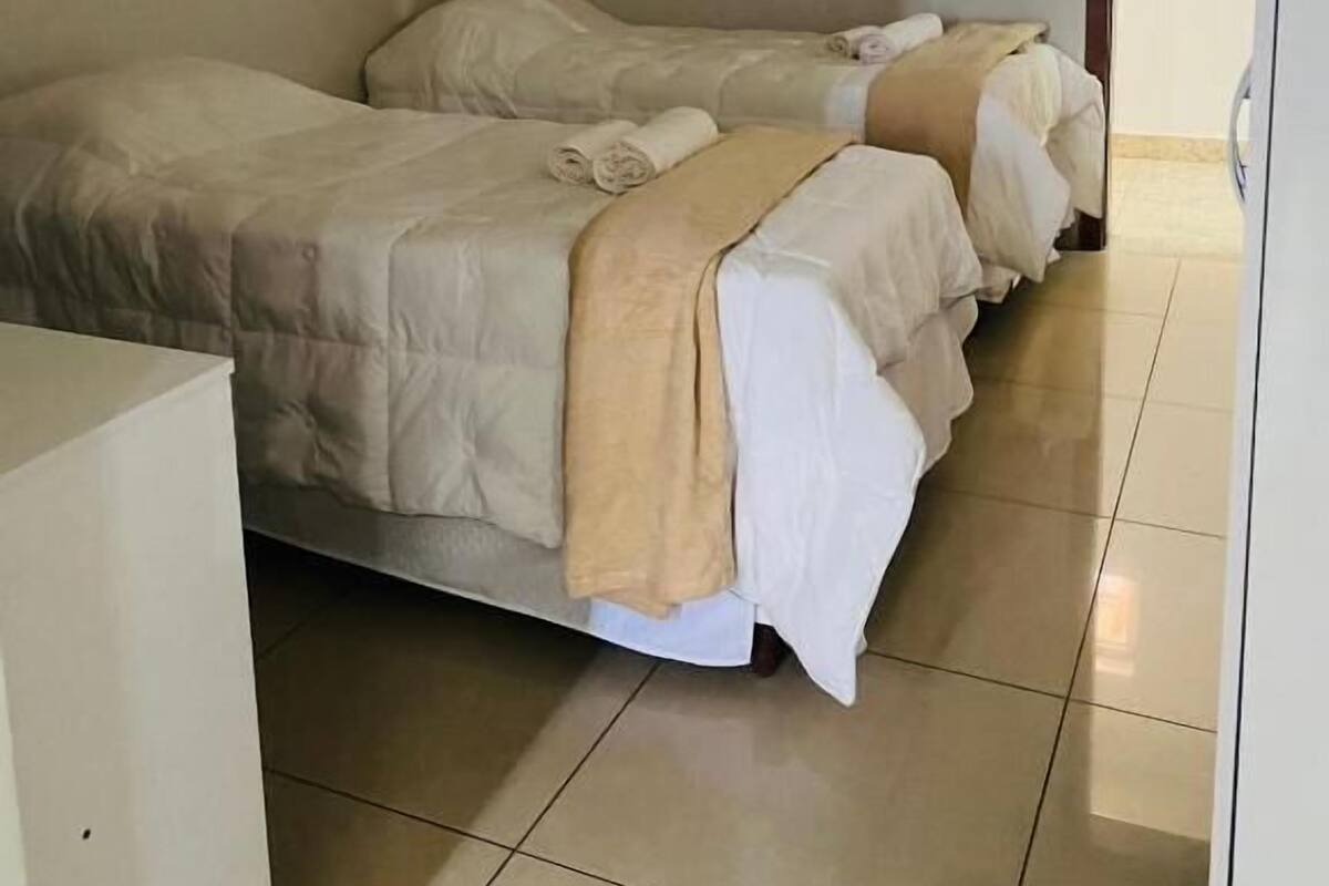 Ein Zimmer mit zwei Betten, jeweils mit einer beigen Decke und Kissen, sowie einem kleinen Tisch im Vordergrund.