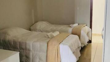 Une chambre avec deux lits, chacun recouvert d’une couverture et de plusieurs oreillers beiges, et une petite table placée au premier plan.