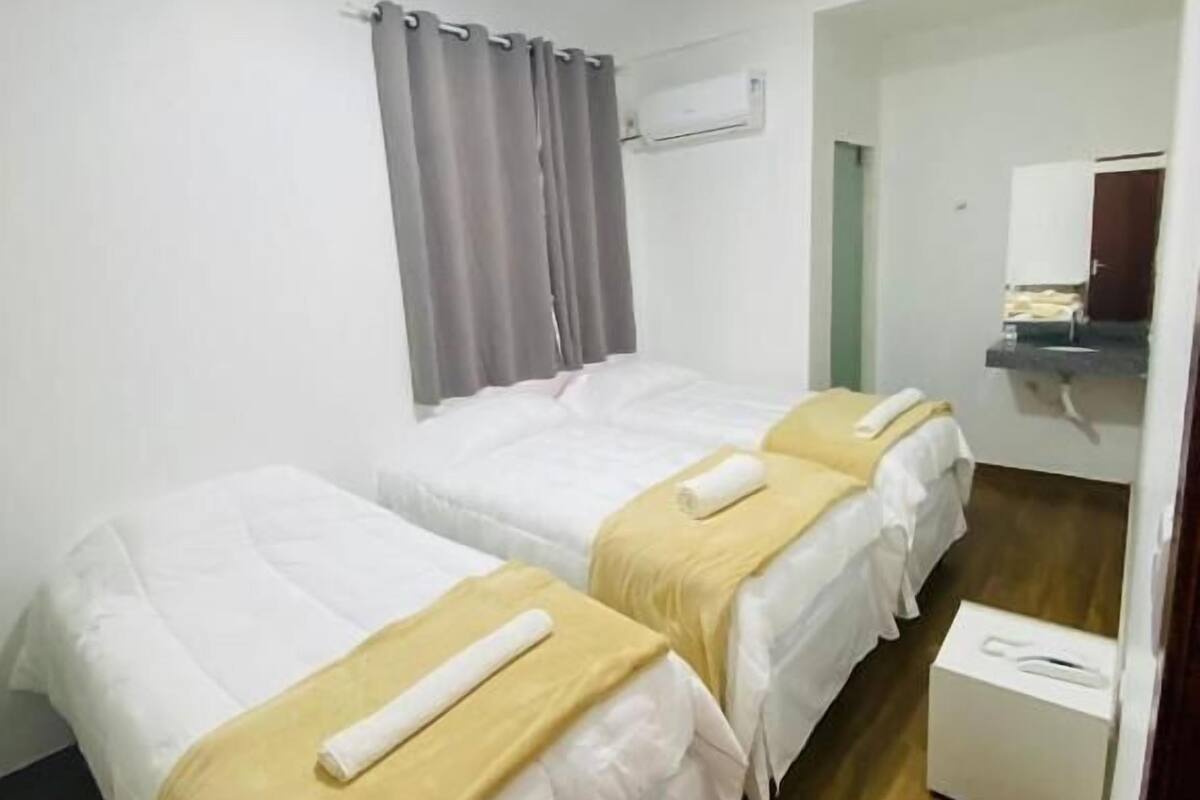 Ein Hotelzimmer mit zwei Einzelbetten, einem kleinen Nachttisch, einem Kleiderschrank, einem Spiegel und einer Wandklimateinheit.