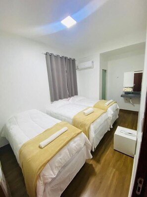 Une chambre d’hôtel avec deux lits simples, une petite table de chevet, une armoire, un miroir et un appareil de climatisation fixé au mur.