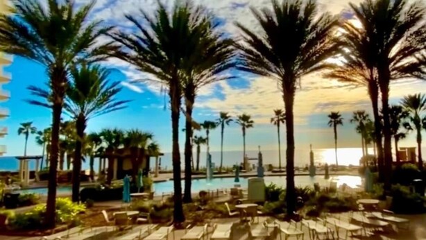 A poolside area with lounge chairs and palm trees, overlooking a body of water. - Gorgeous Sunset Condo at One of the Most Beautiful Pool Resorts on the Beach!  (Panama City Beach)