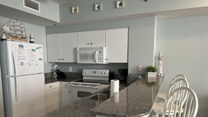 A modern kitchen with white cabinets, a granite countertop, a built-in microwave, and a stove. - Gorgeous Sunset Condo at One of the Most Beautiful Pool Resorts on the Beach!  (Panama City Beach)